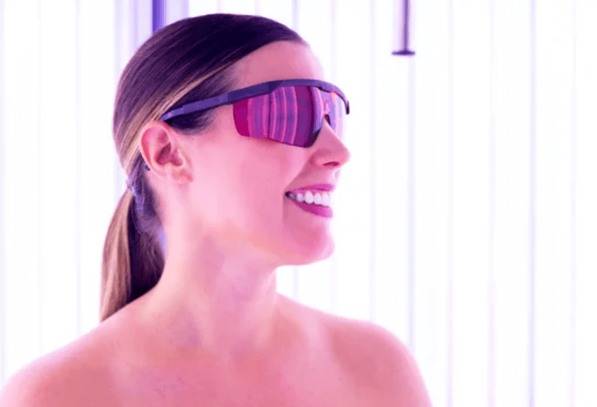Una ragazza sorridente che indossagli occhiali protettivi all'interno di una doccia abbronzante